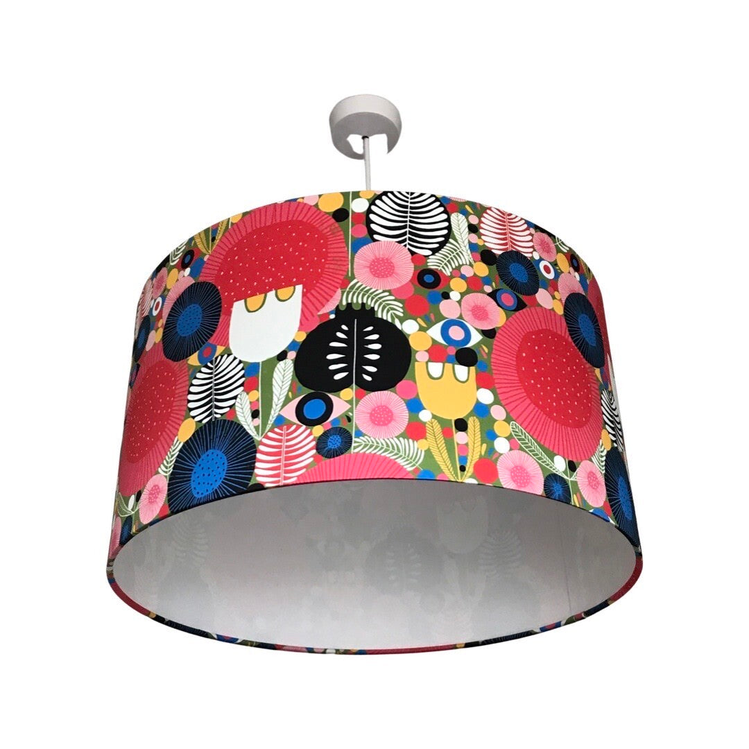 Drum lampshade covered in cotton sateen mid-century inspired fabric with various flowers and leaves in reds, white, yellow, red, pinks, greens and blues.