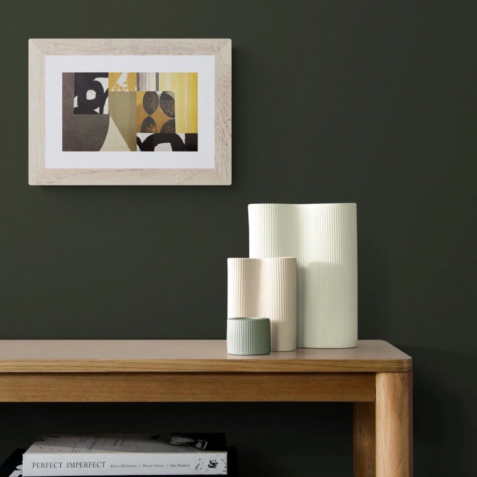 Abstract print framed on a green wall, next to a table with large ornaments.