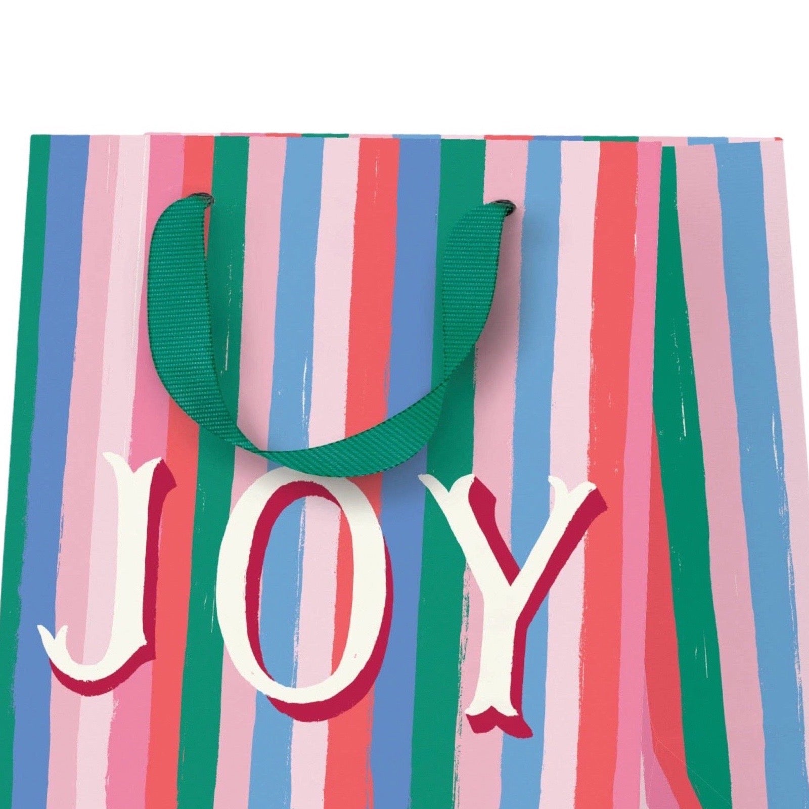 A striped gift bag with vertical pink, blue, green, and white brushstroke-style stripes, featuring a dark green ribbon handle and the word "JOY" in large white letters with red outlines across the front.