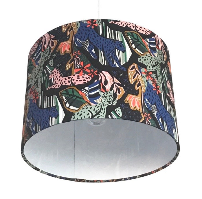 Close up of a drum lampshade with pink, blue and green jungle cats and jungle foliage against a black background