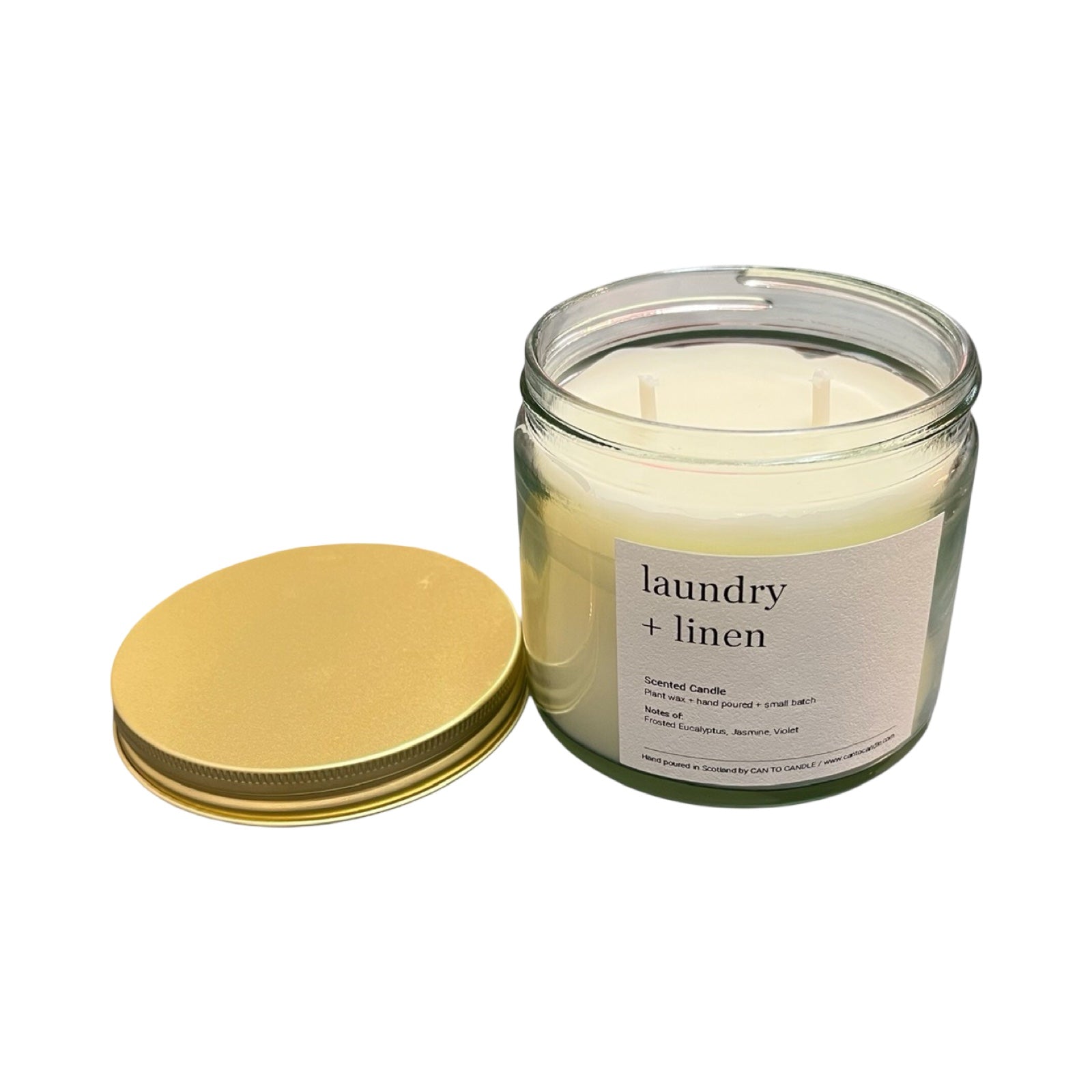 Glass candle labeled 'laundry + linen' with a gold lid on a white background.