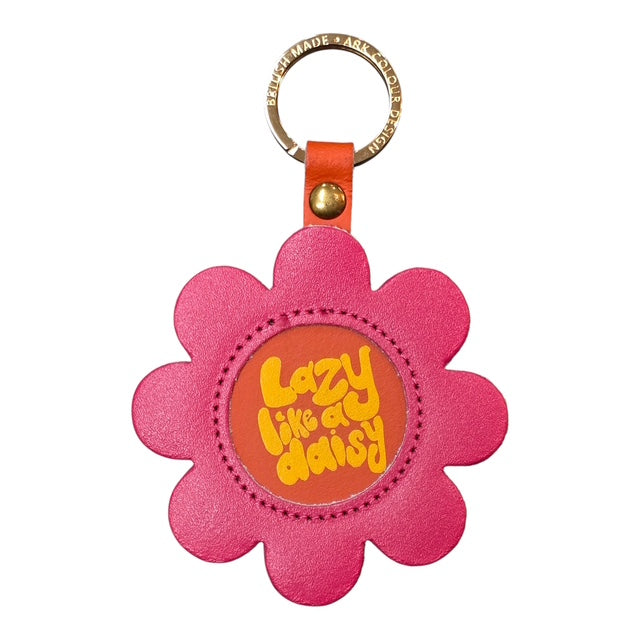 A pink flower-shaped keyring with an orange centre and the text lazy like a daisy' written in the centre.in yellow.