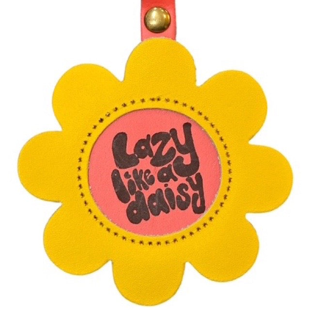 Yellow flower-shaped keychain with 'Lazy Like a Daisy' text on a pink background.