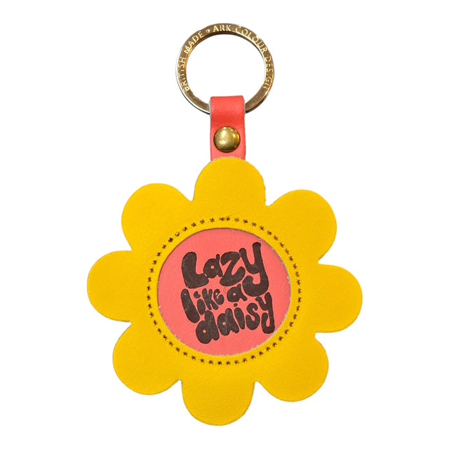 A yellow flower-shaped keyring with a coral coloured centre and the text lazy like a daisy' written in the centre.in brown.