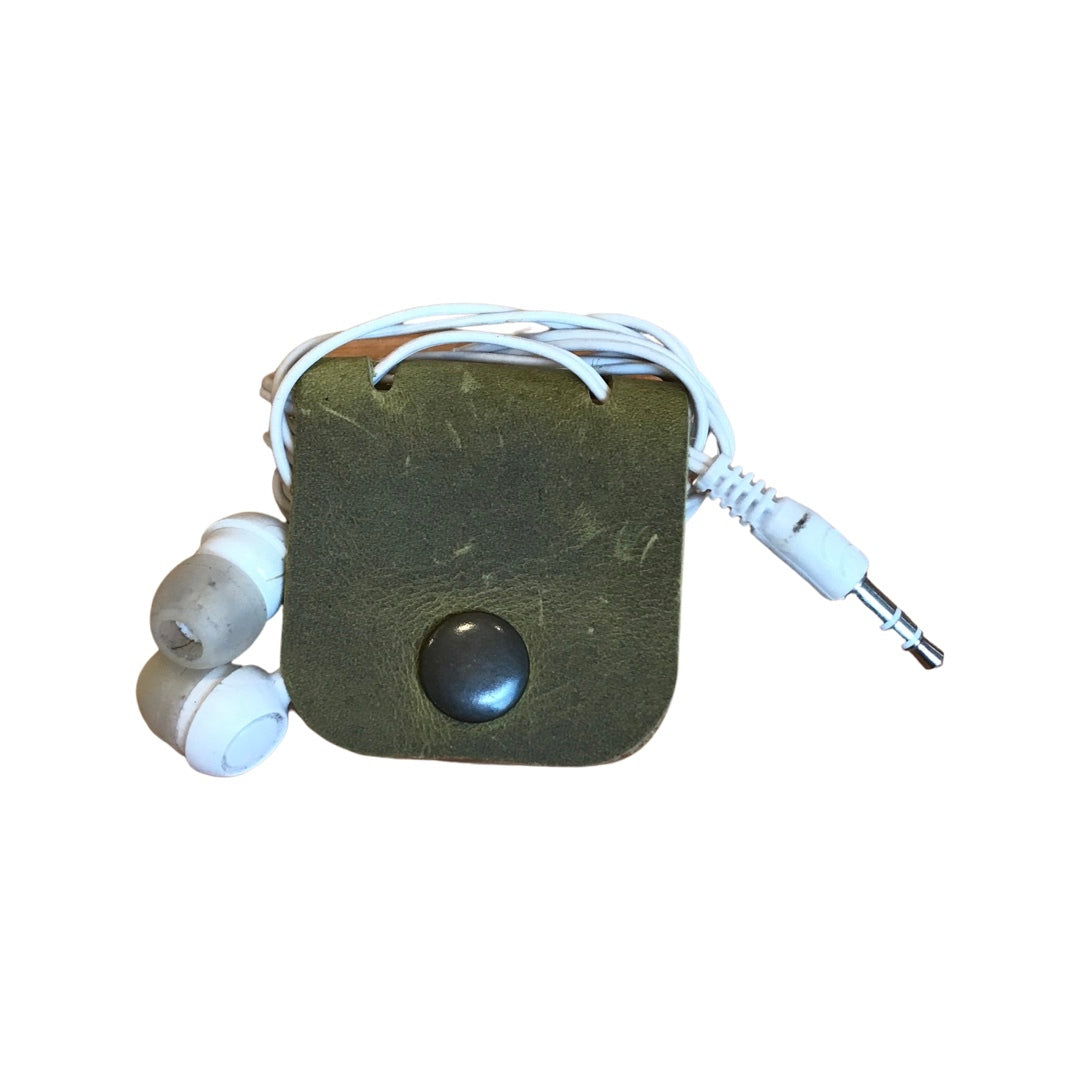 A leather cable organiser in green, closed with a white cable and earphones partially inserted.