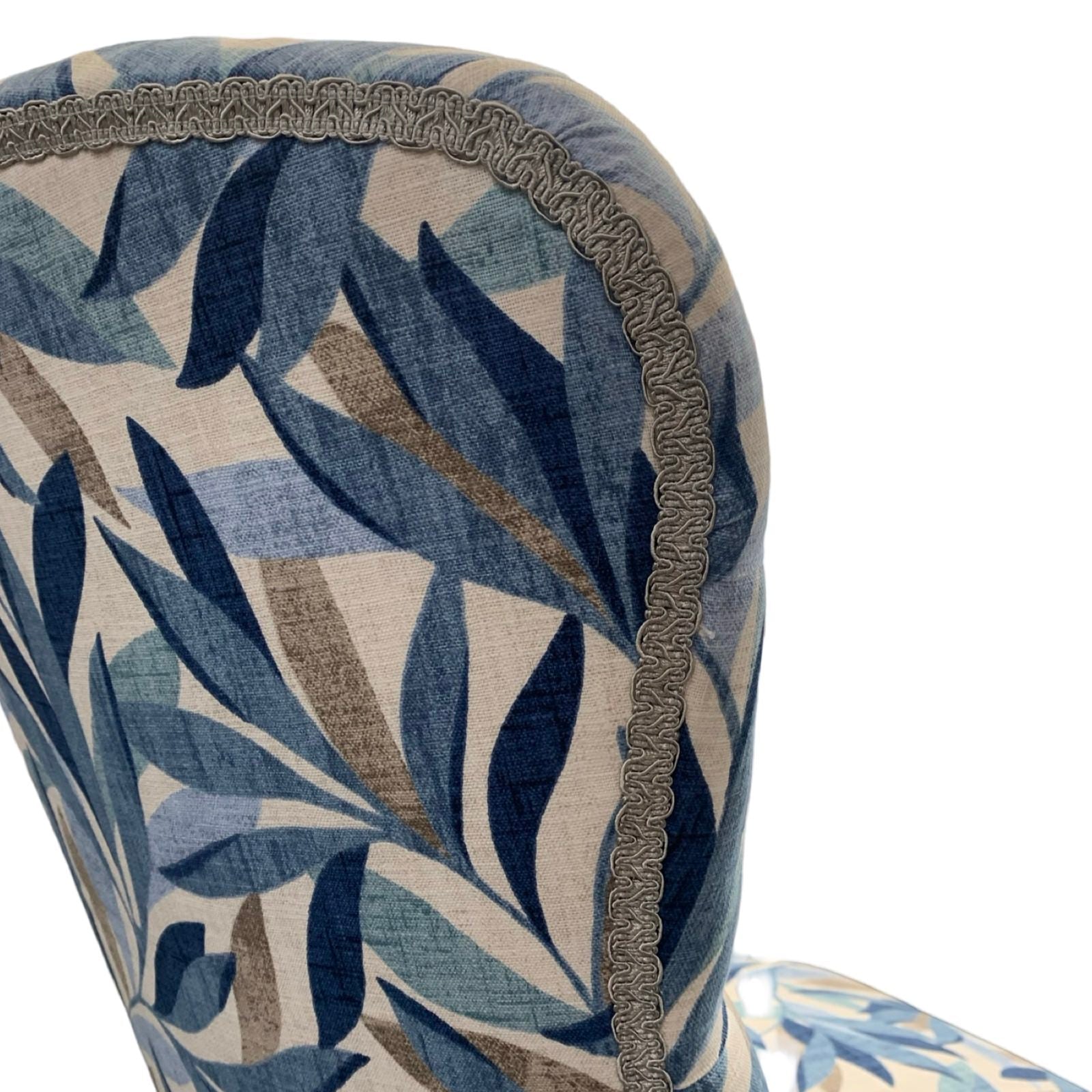 A blue linen armchair with a leaves pattern, featuring button-back tufting and oak legs with gold castors.