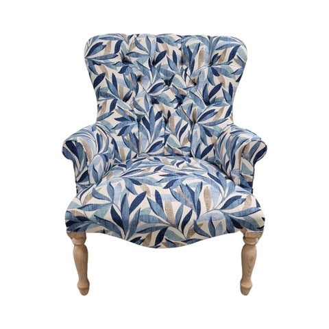 A blue linen armchair with a leaves pattern, featuring button-back tufting and oak legs with gold castors.