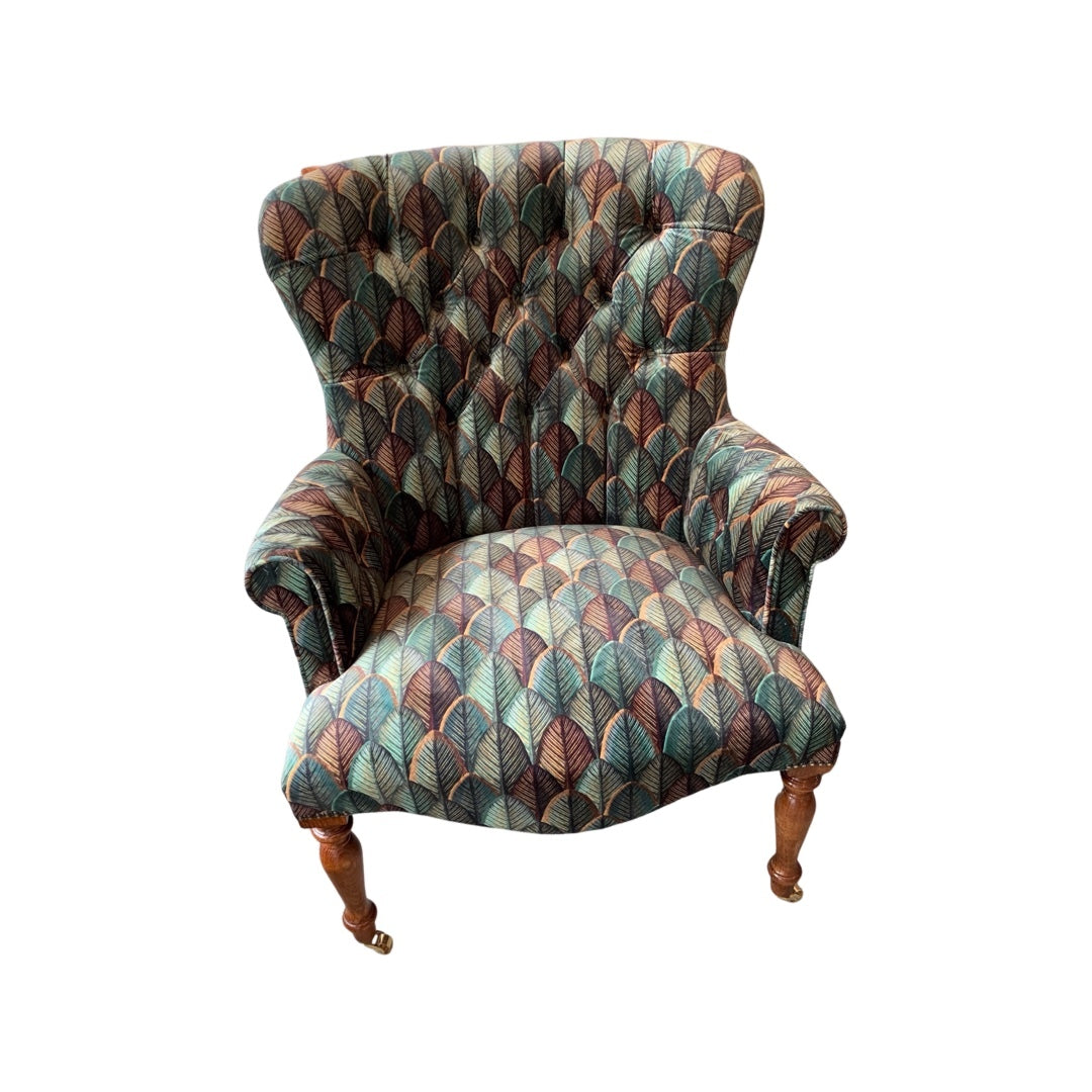 A hand-crafted armchair with a leaf design in soft velvet, featuring a button-back, mahogany legs, and gold castors.