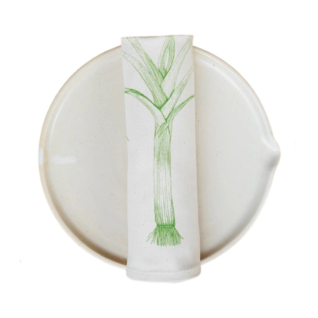 Cream cotton napkin with a green leek rolled on a plate.