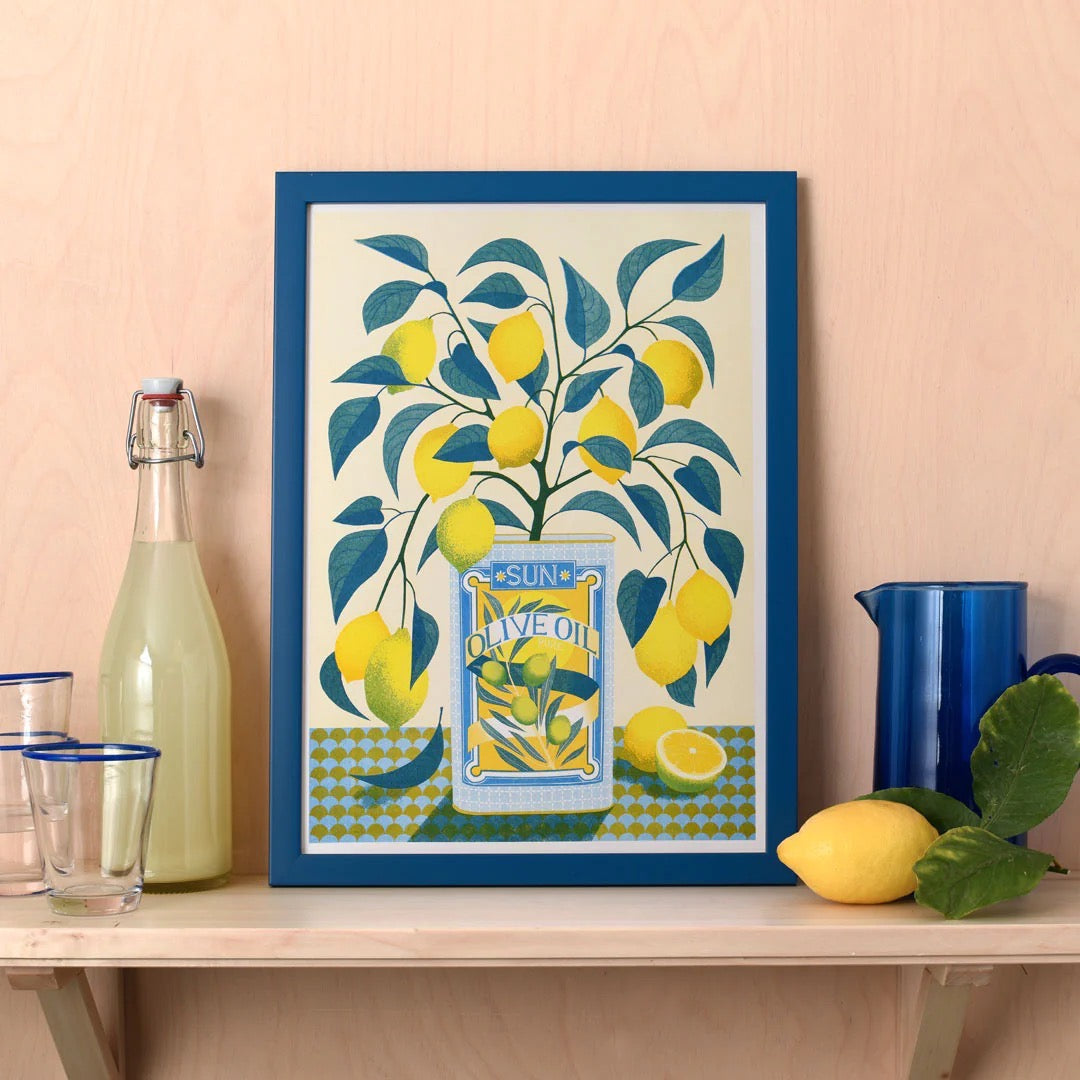 Framed artwork of lemons and a bottle on a table against a pink wall.