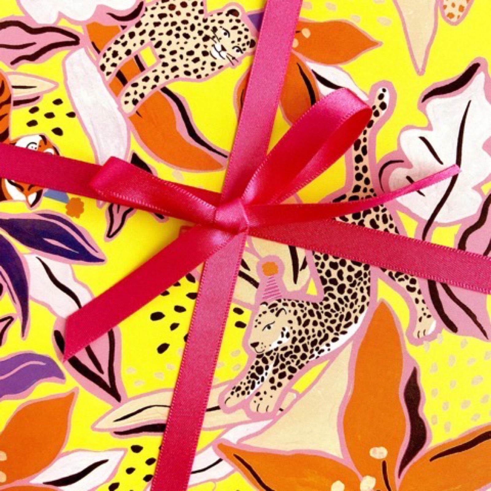 Wrapping paper featuring black and white leopards surrounded by orange, lilac and white flowers on a yellow background.