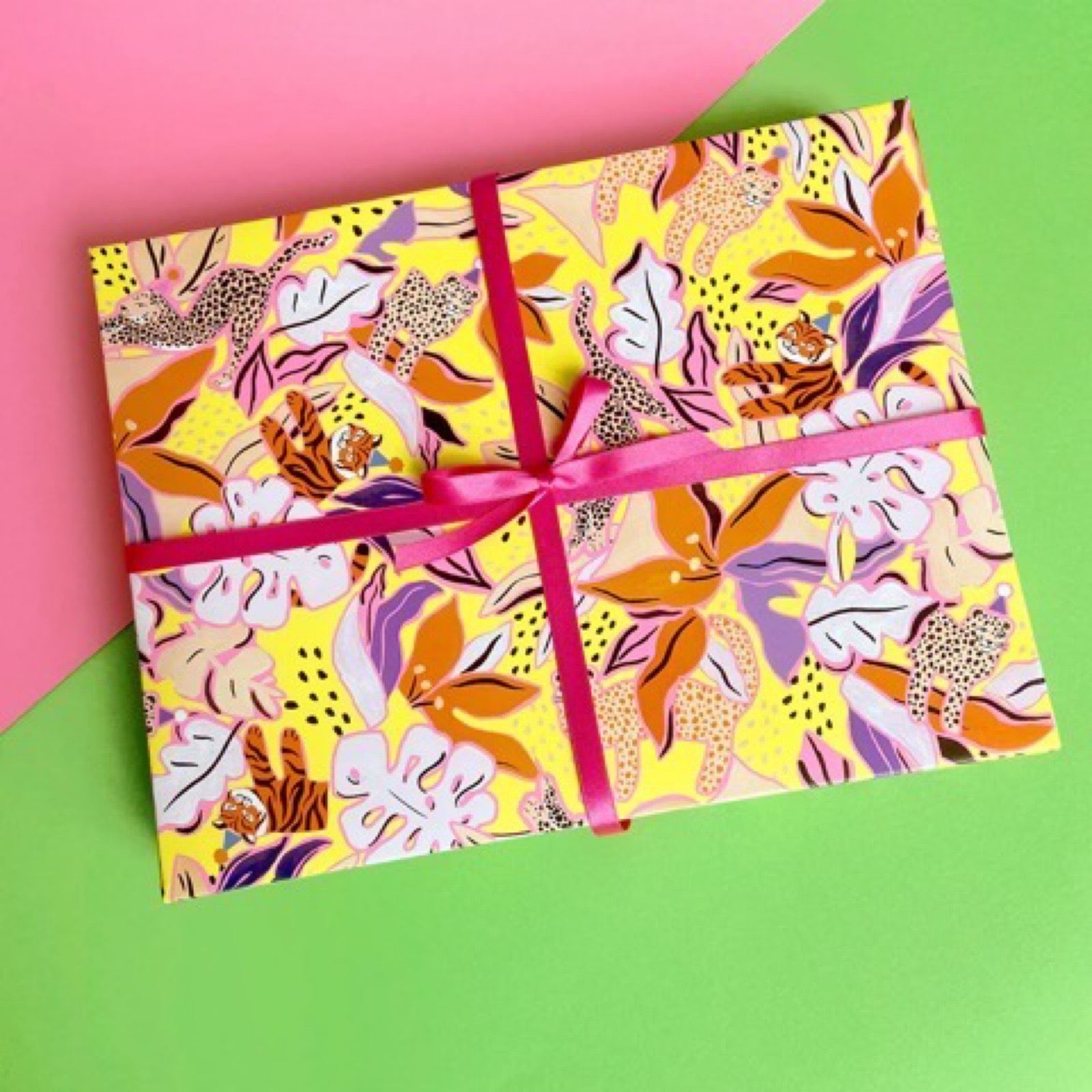 Wrapping paper featuring black and white leopards surrounded by orange, lilac and white flowers on a yellow background.