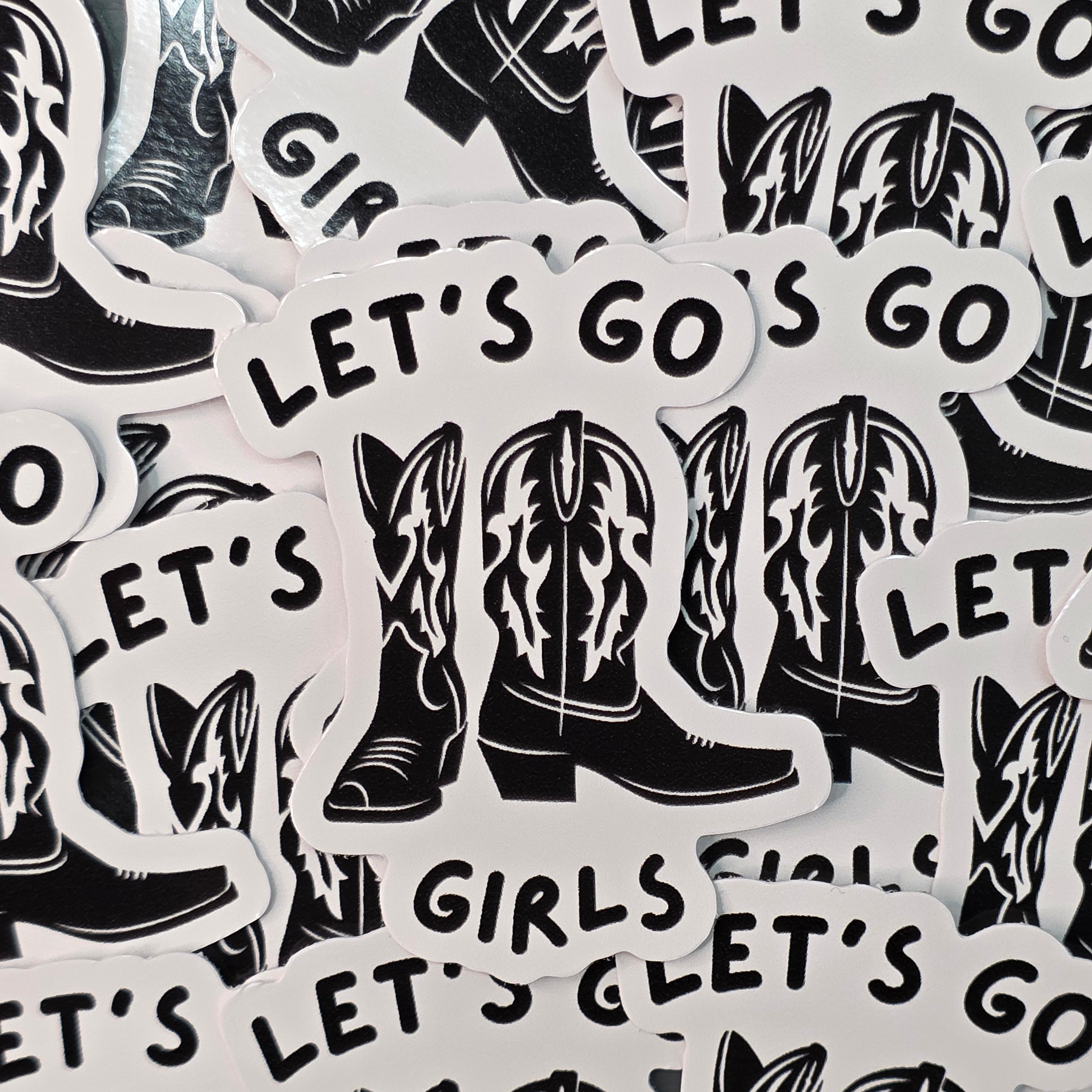 A waterproof vinyl sticker of a black pair of cowboy boots and the text 'Let's Go Girls' in black.