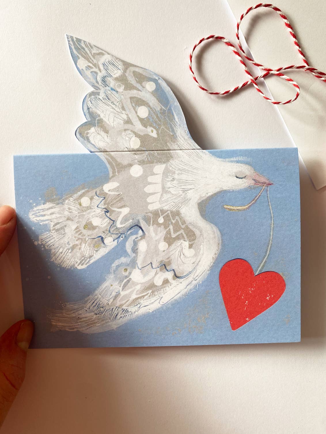 Card with a dove and red heart on a light blue background, held by a hand.