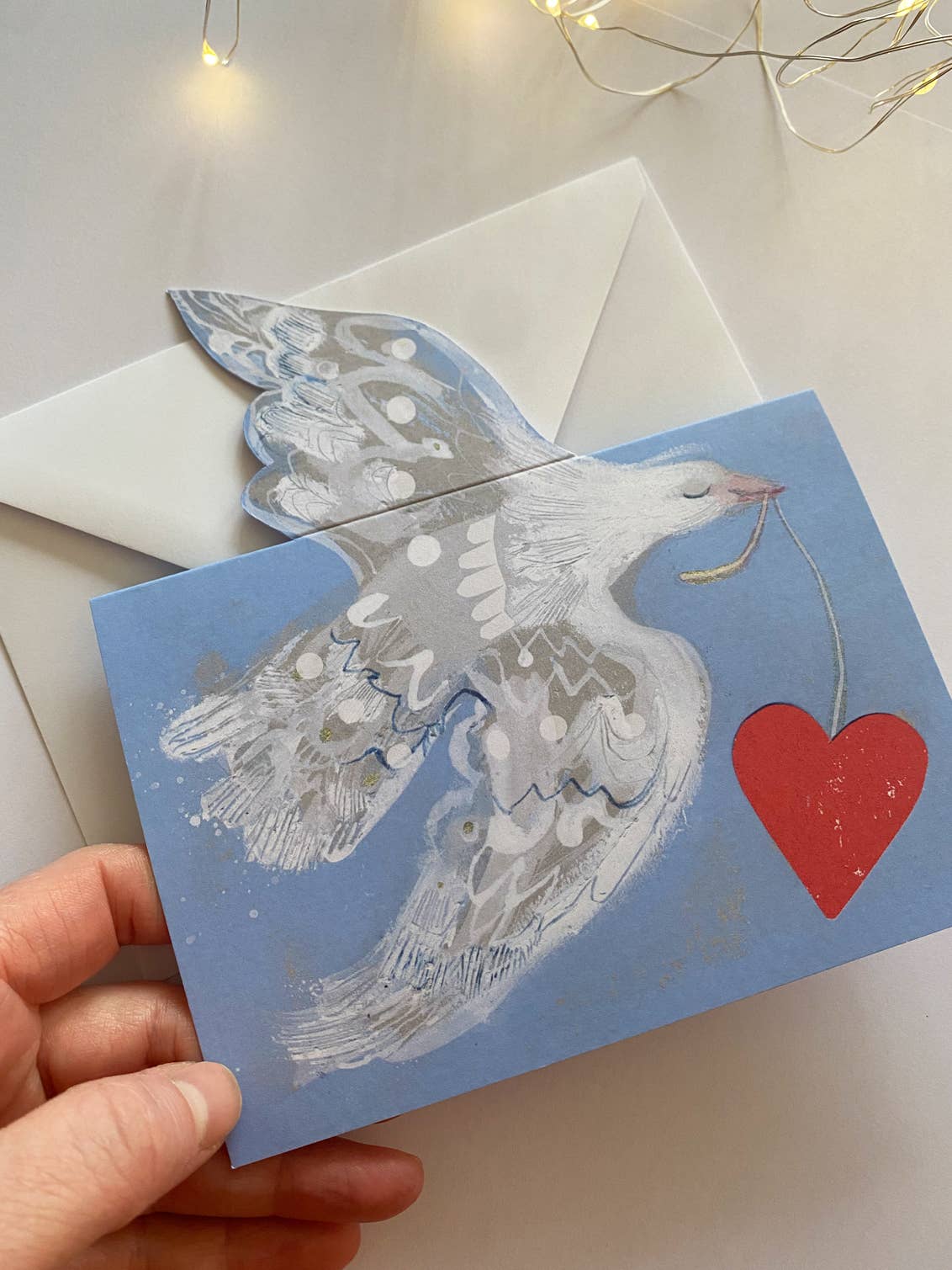Card with a dove and heart design held by a hand on a light background.