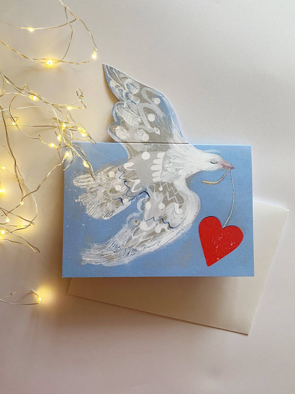 Greeting card with a dove and heart design on a light background with string lights.