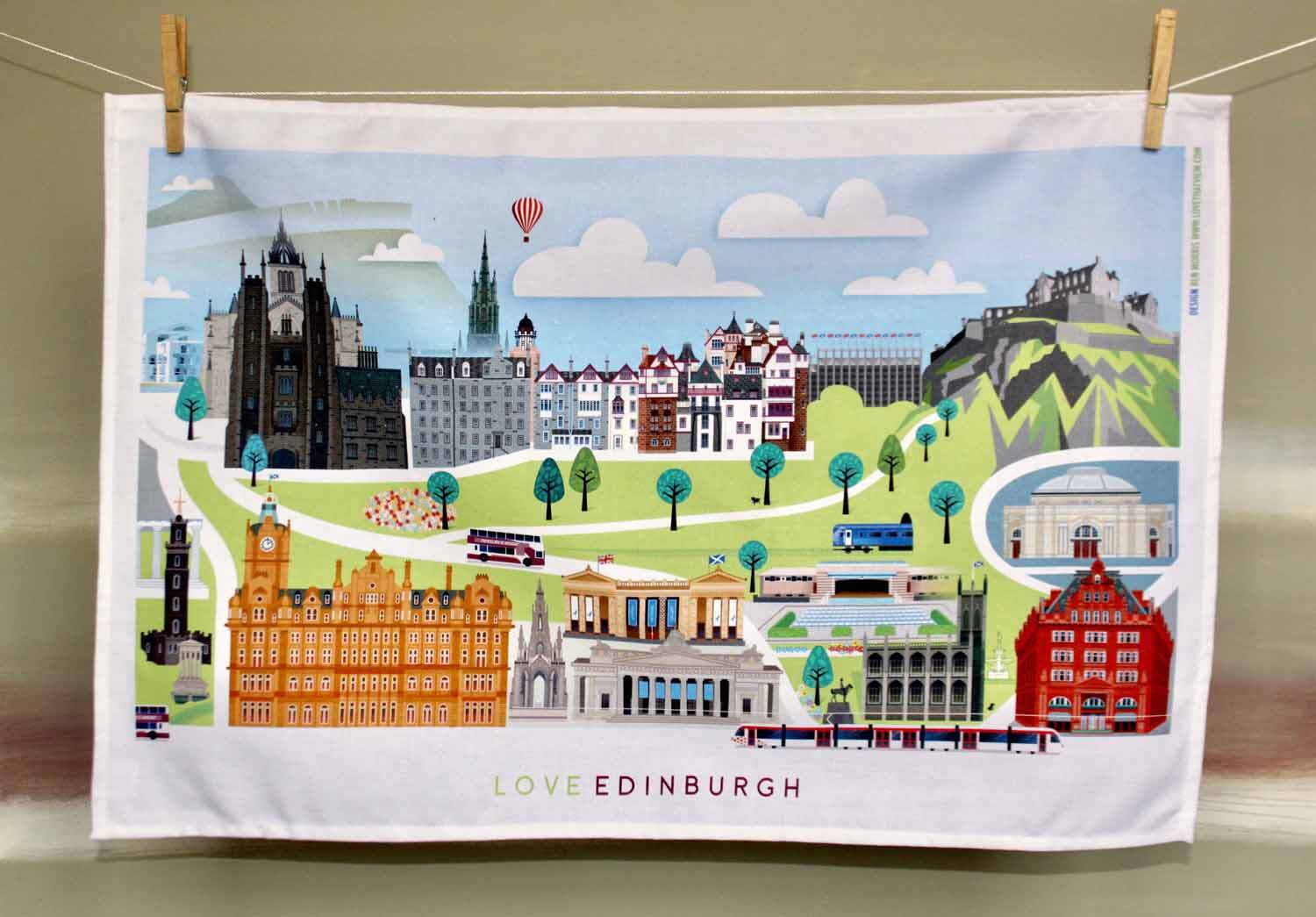 An open cotton tea towel with an illustration of various famous landmarks in Edinburgh, including a hot air balloon and a map outline.