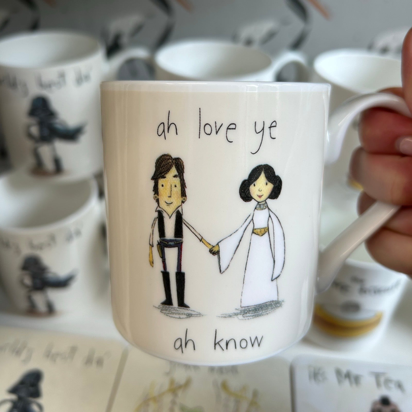 Mug with illustrations of a couple and text 'ah love ye, ah know' held by a hand.