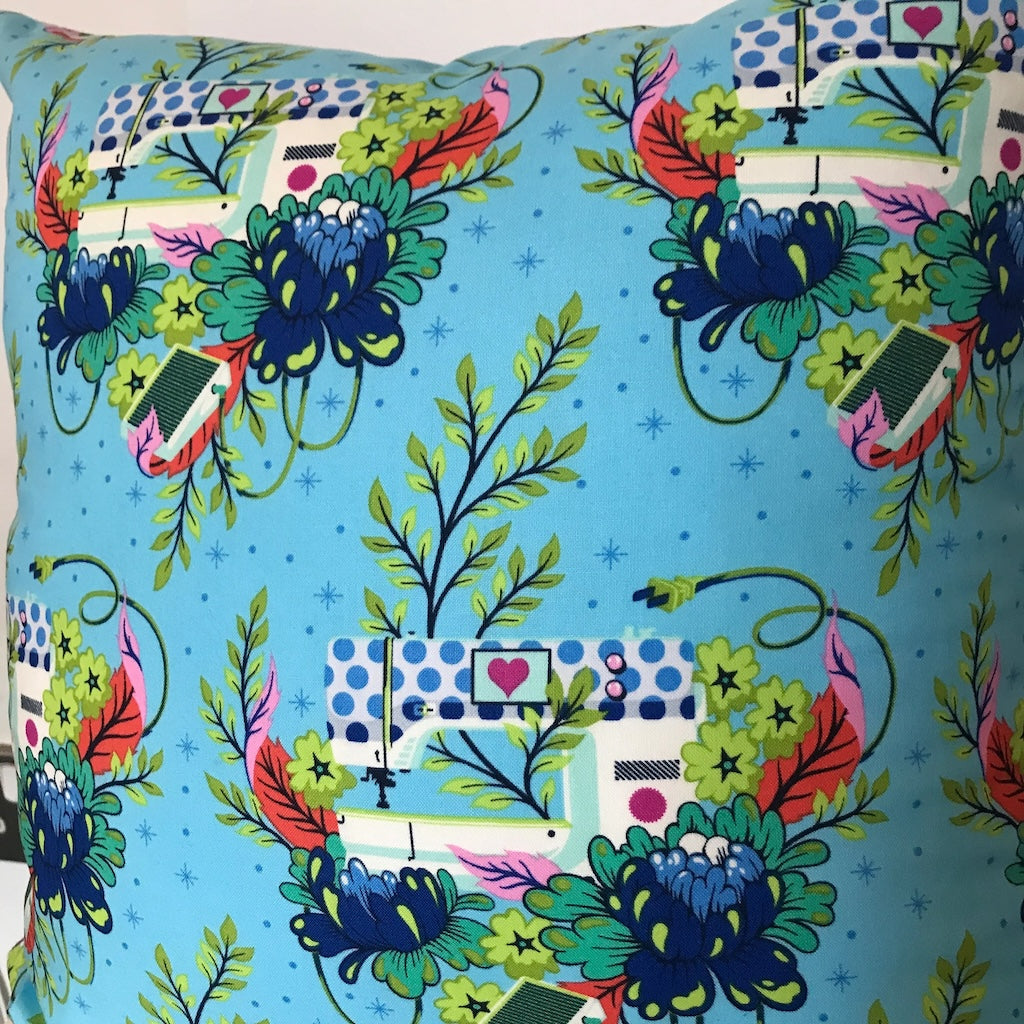 A cushion cover with a turquoise background and a pattern featuring sewing machines and flowers.