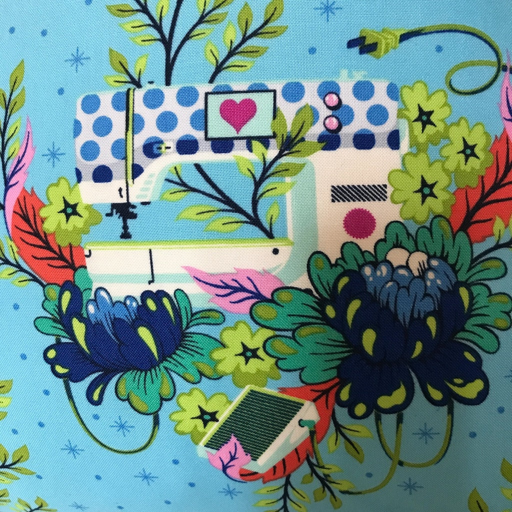 A cushion cover with a turquoise background and a pattern featuring sewing machines and flowers.