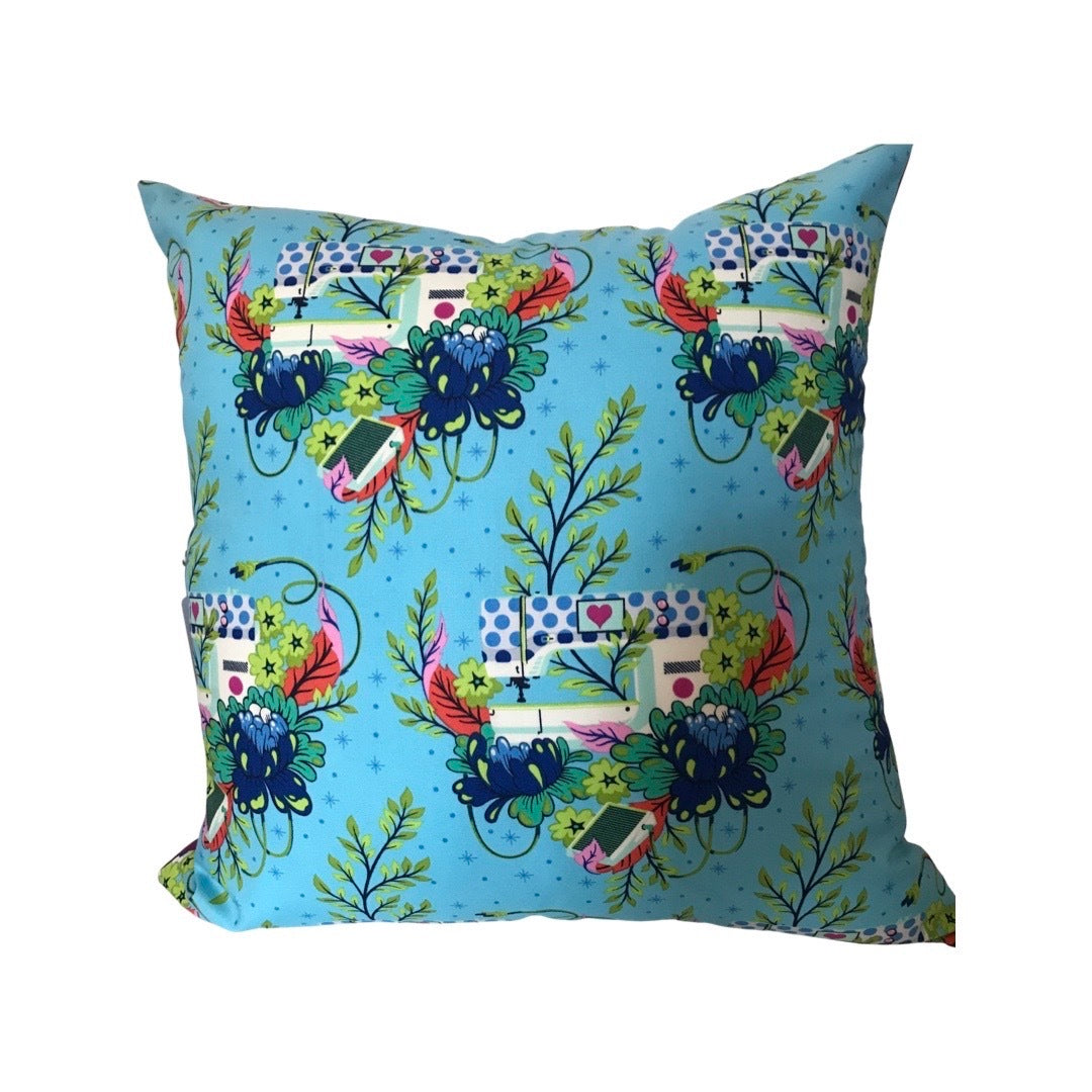 A cushion cover with a turquoise background and a pattern featuring sewing machines and flowers.