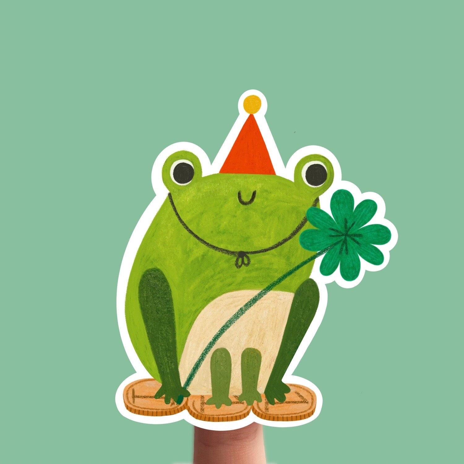 Illustration of a frog wearing a party hat and holding a four-leaf clover on a green background.