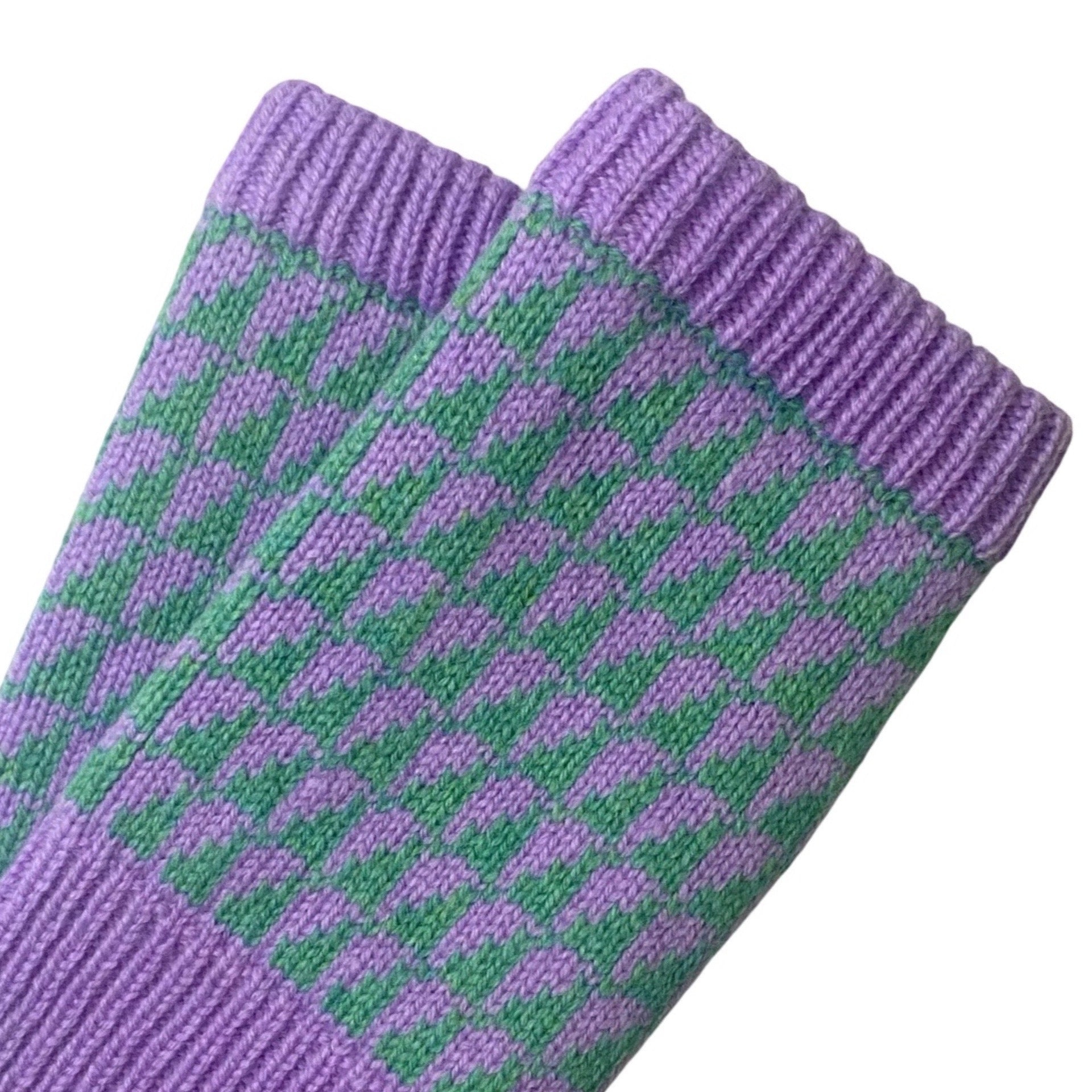 A close-up of a pair of purple and green patterned knit wrist warmers on a plain white background.