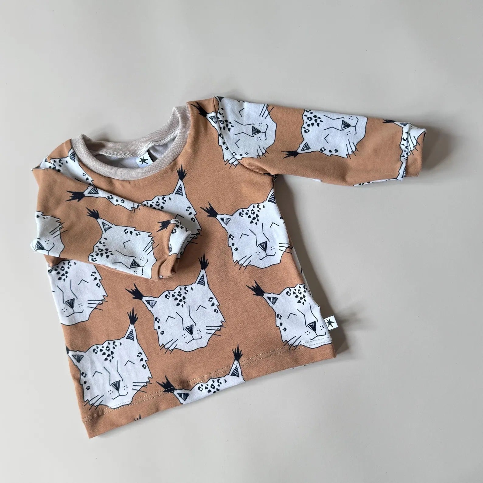 A long-sleeved brown baby t-shirt with a lynx pattern and little cuffs.