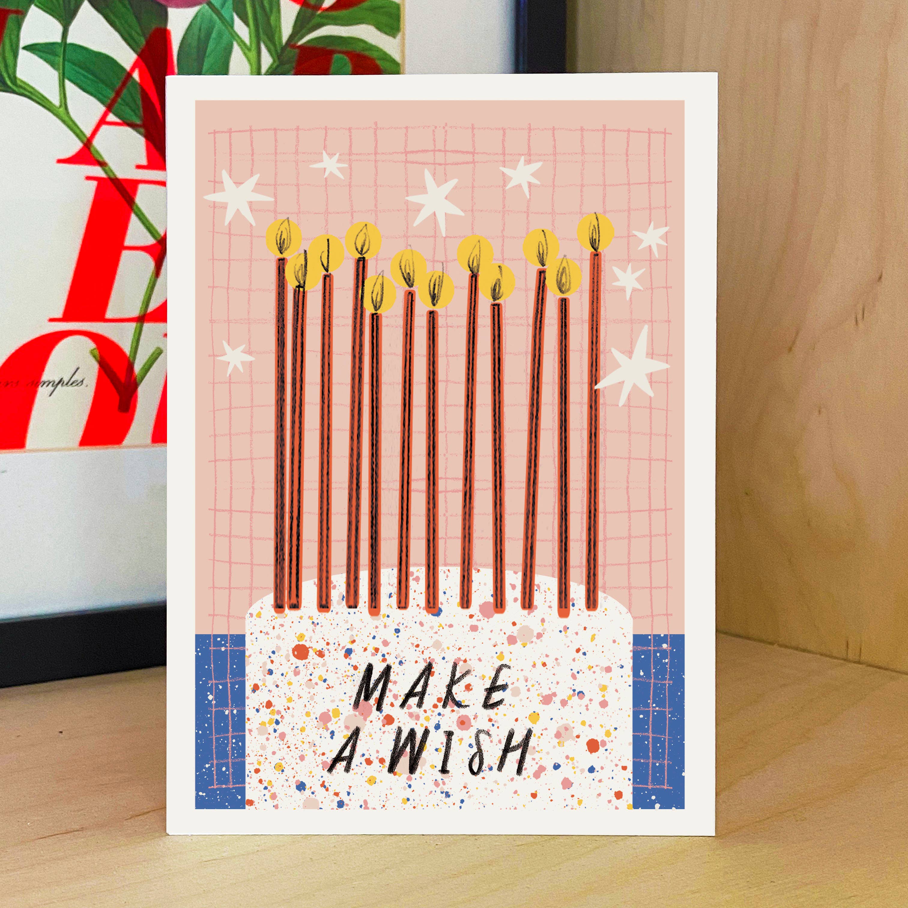 Greeting card with lit candles and 'Make a Wish' text on a wooden background.