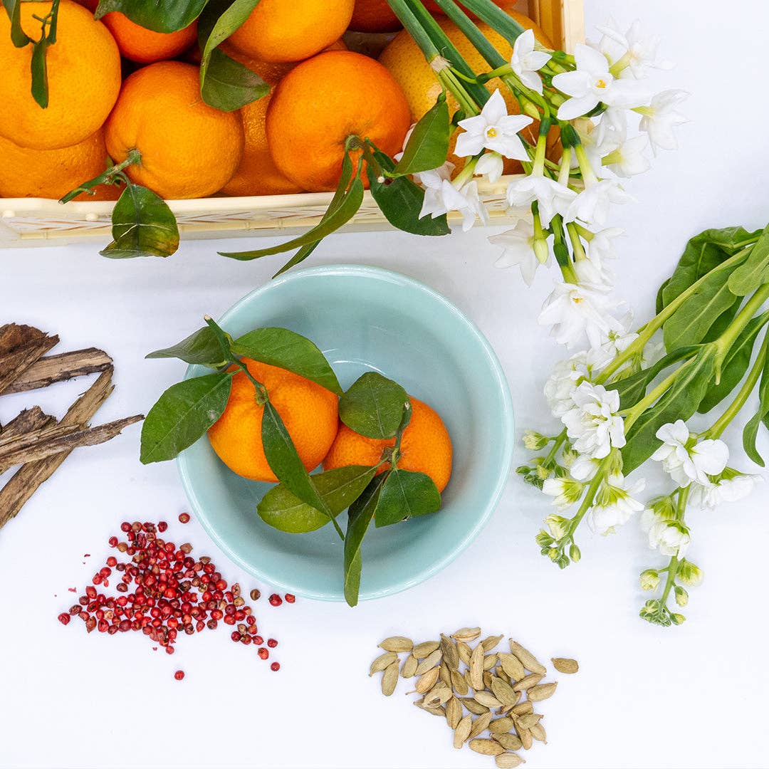Oranges in a bowl with flowers, leaves, and seeds on a white background
