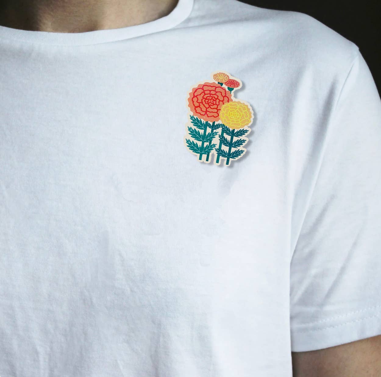 A close-up of a person wearing a white short-sleeve t-shirt with a colourful brooch of flowers on the left chest.
