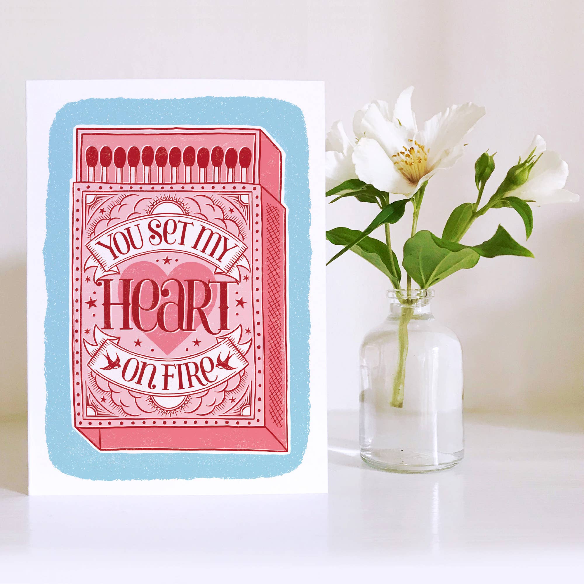 Greeting card with romantic message next to a vase with flowers on a white background.