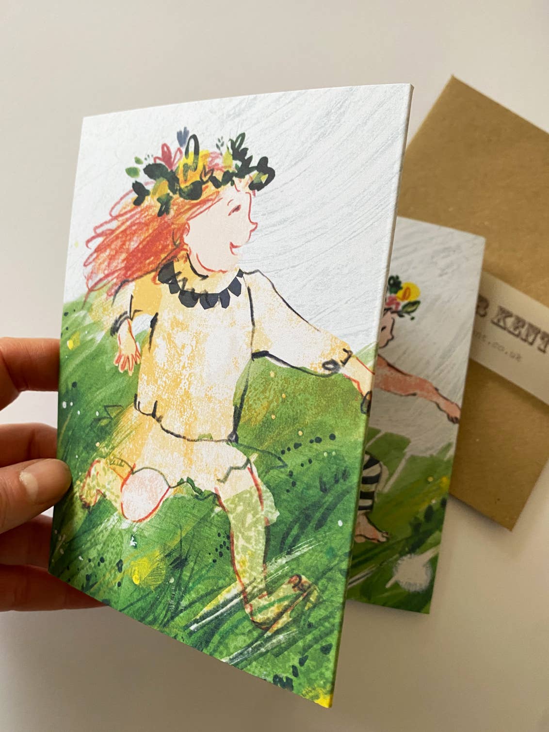 Hand holding a greeting card with a colorful illustration of a person in nature-themed attire.