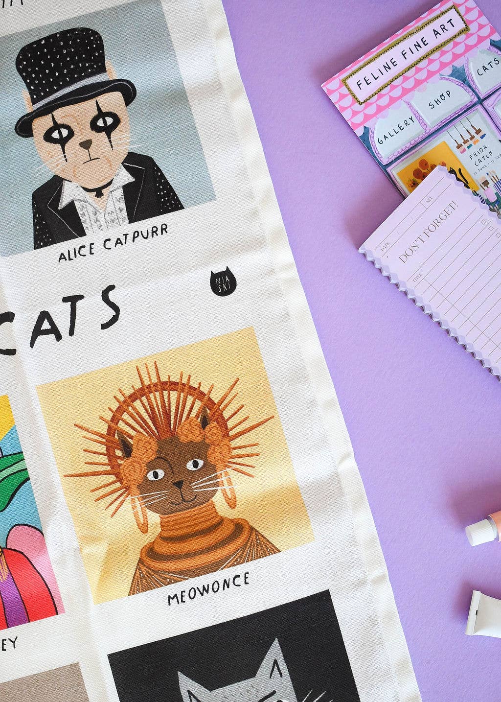 Cat-themed products including a notebook, stickers, and a decorative item on a purple background.