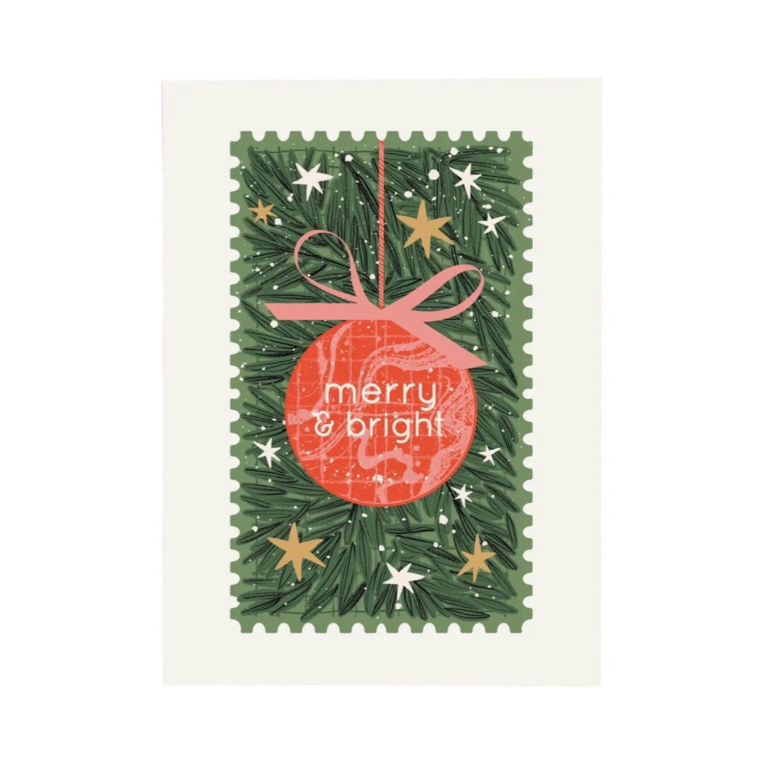 Christmas card featuring a red and pink hanging bauble with a pink bow and the text 'merry and bright' in the centre, all against a background of green pine needles