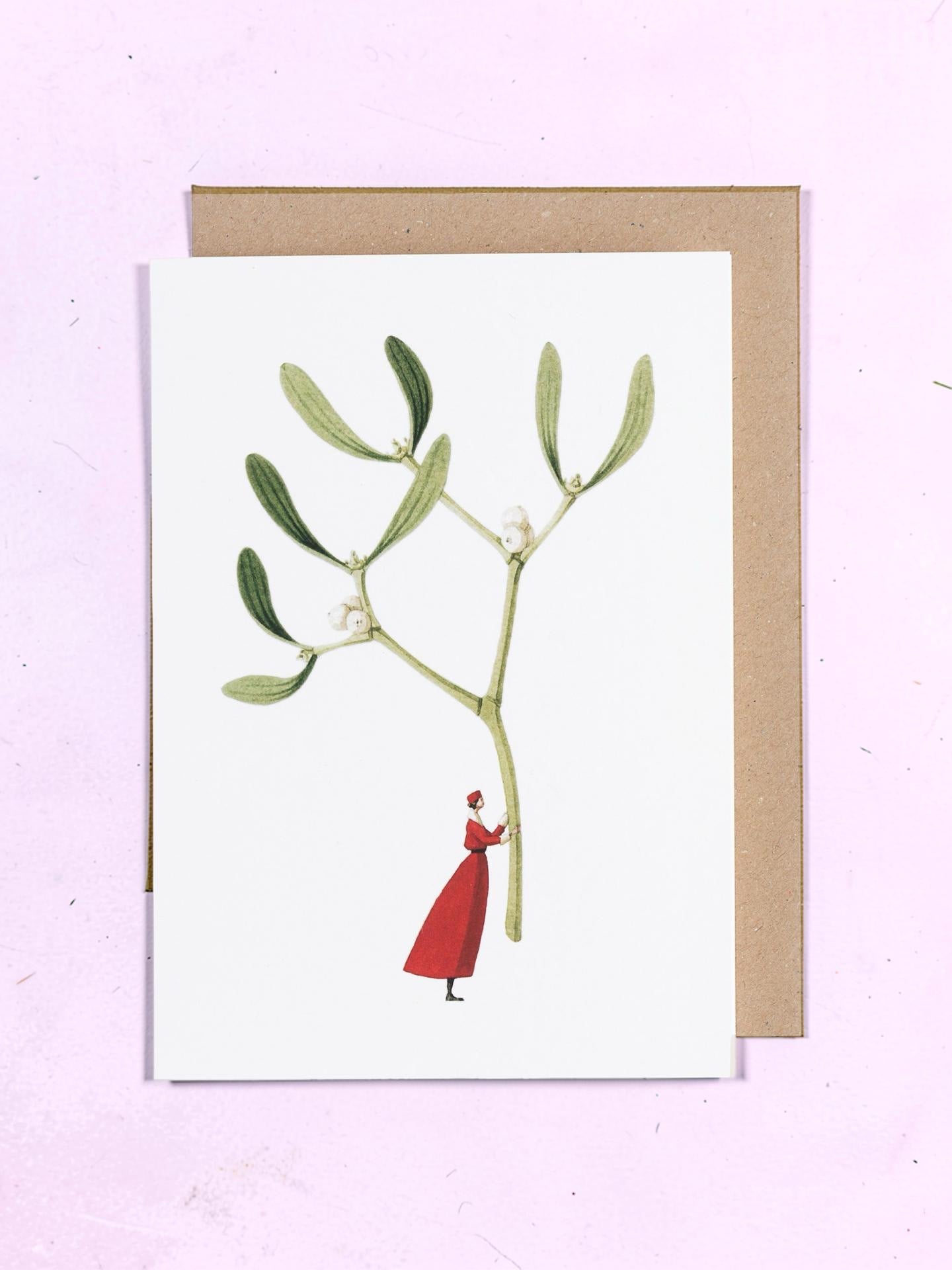 Greeting card with illustration of a person in a red coat holding with a mistletoe plant on a pink background.