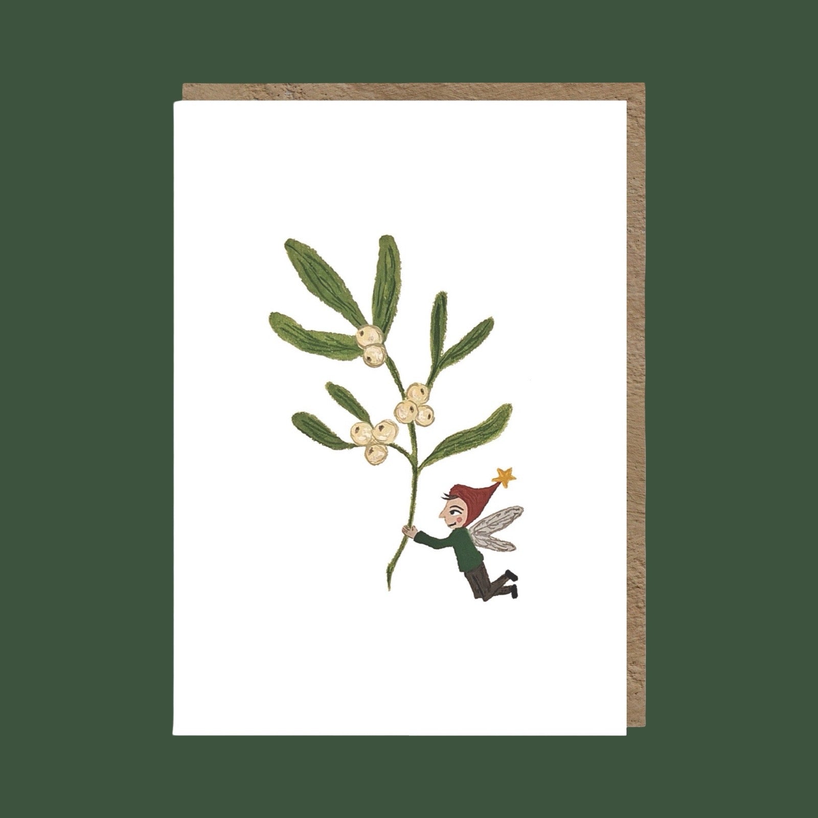 A white greeting card with a brown envelope, featuring an illustration of a mistletoe branch with small white berries and a tiny fairy in a red hat reaching for it, set against a dark green background.
