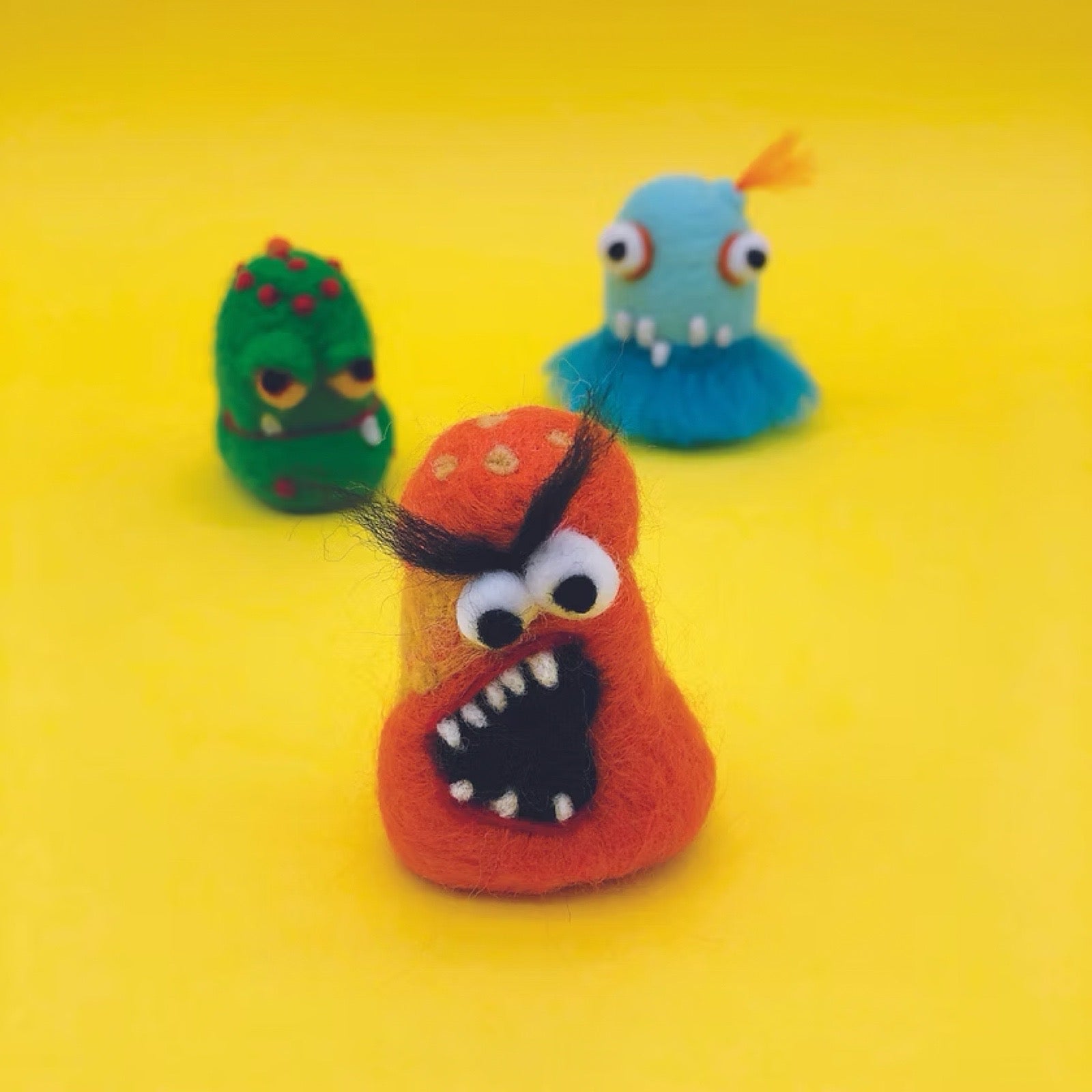 Three colourful felt monsters on a yellow background.