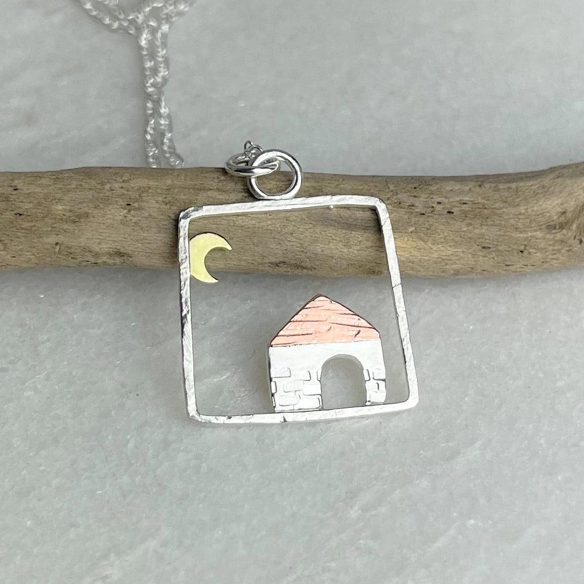 Silver pendant with a house and moon design on a gray surface.