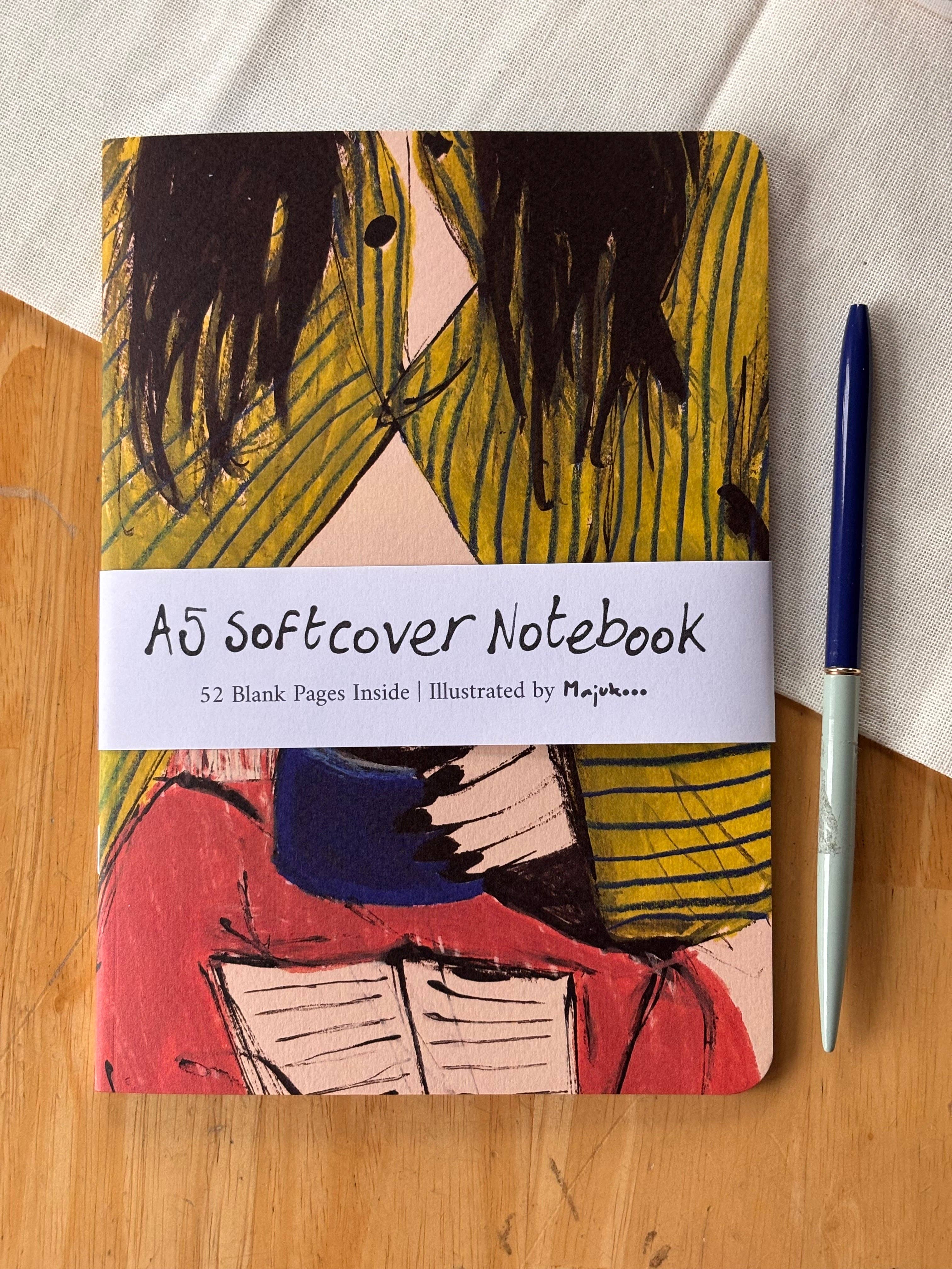 A5 softcover notebook with artistic cover design on a wooden surface.