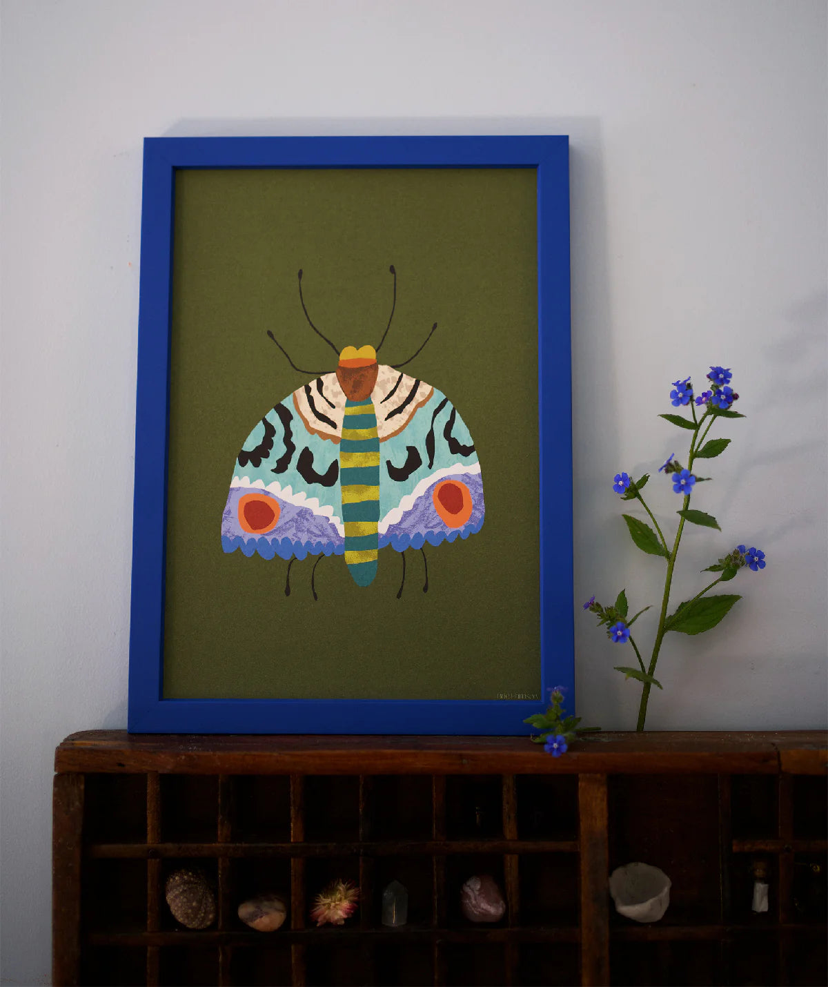 Framed artwork of a colourful butterfly on a green background, displayed on a wooden shelf with decorative items.