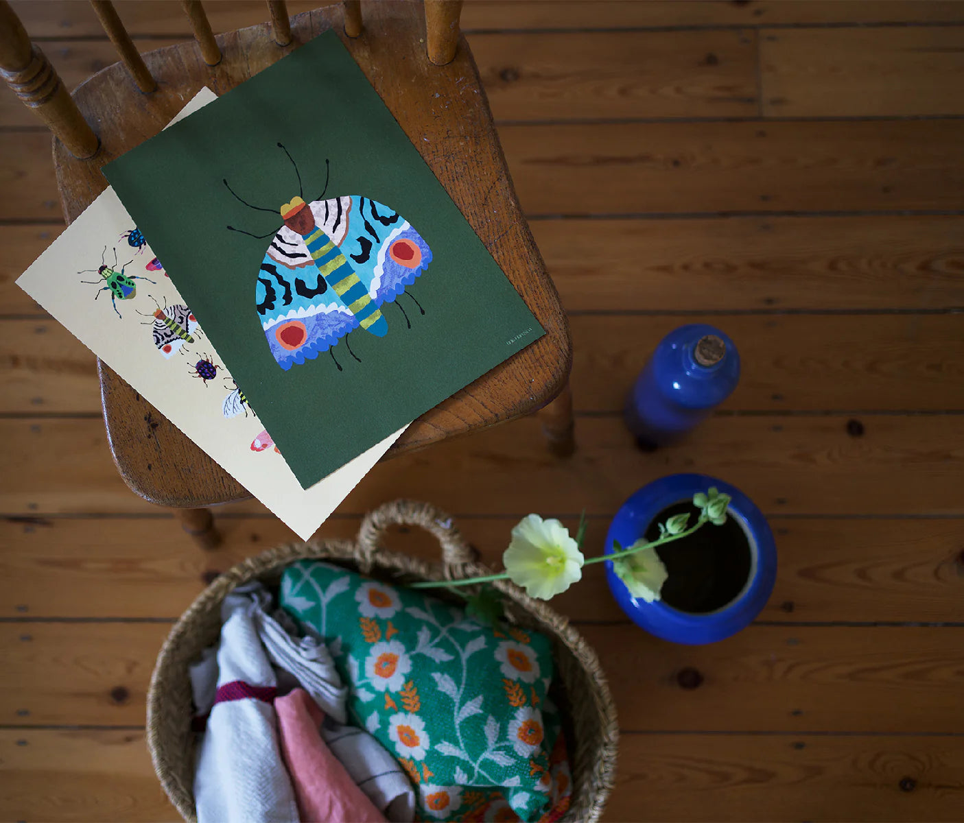 Wooden chair with a colourful butterfly painting, a basket of clothes, and a blue container on a wooden floor.