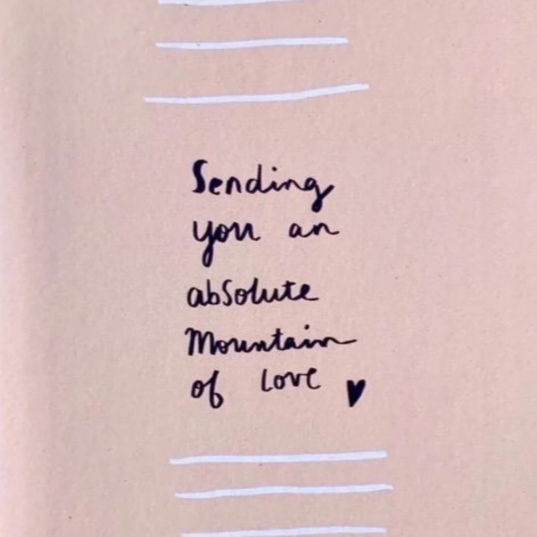 A sympathy card with a pale pink background, featuring the text 'SENDING YOU AN ABSOLUTE MOUNTAIN OF LOVE' in black, accompanied by a small black heart, and lined with a striped pattern.