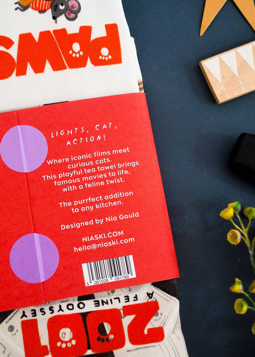 Close up of tea towel packaging with text, on a table with stationary items.