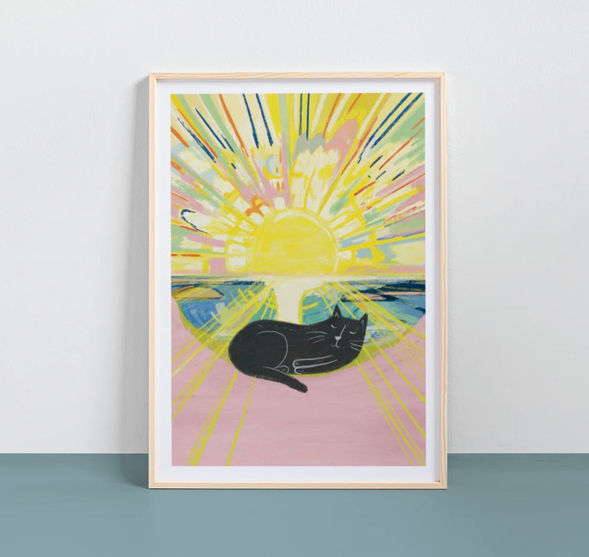 Framed artwork of a black cat under a colorful sun on a white wall.
