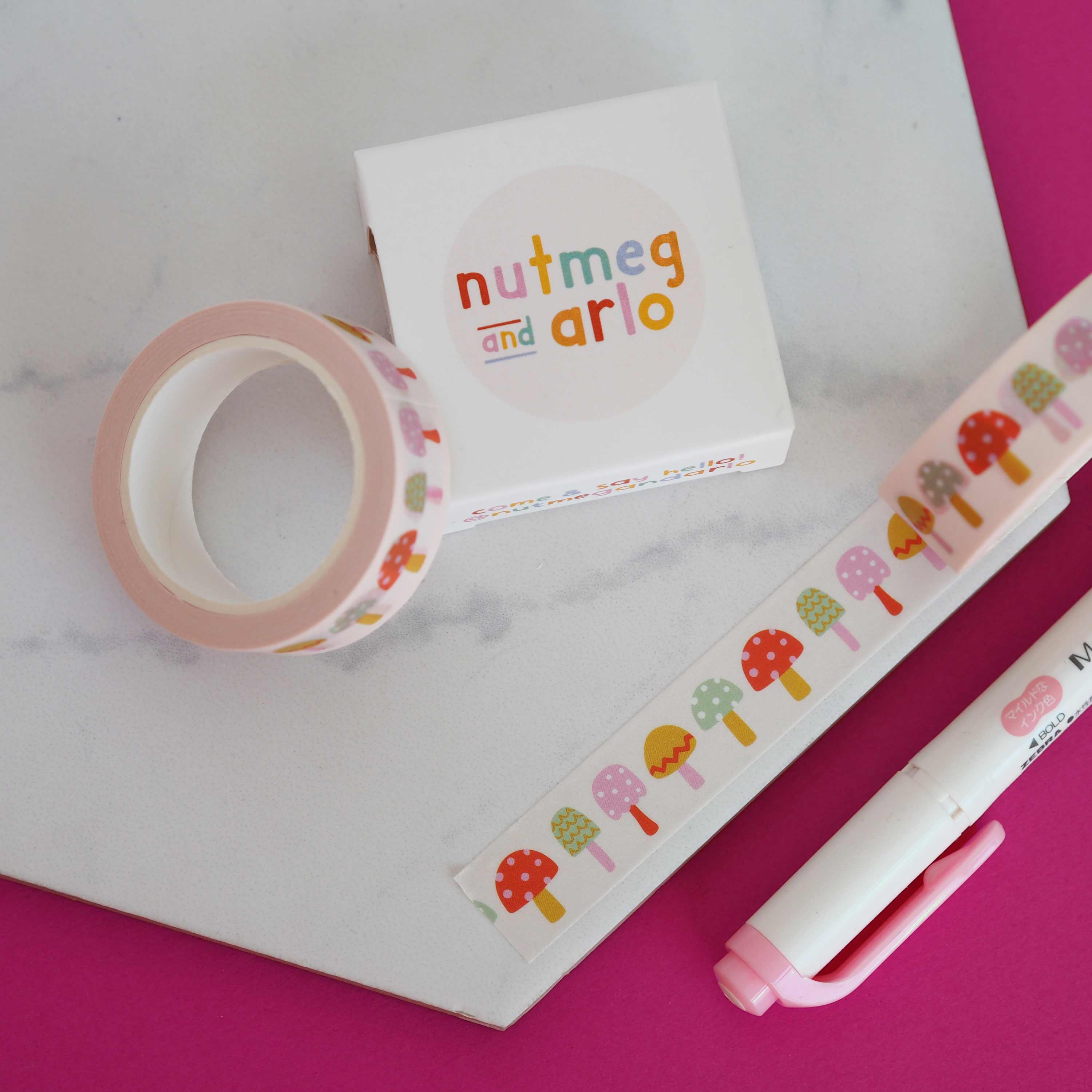 Colorful washi tape, notebook, and pen on a pink and white background.