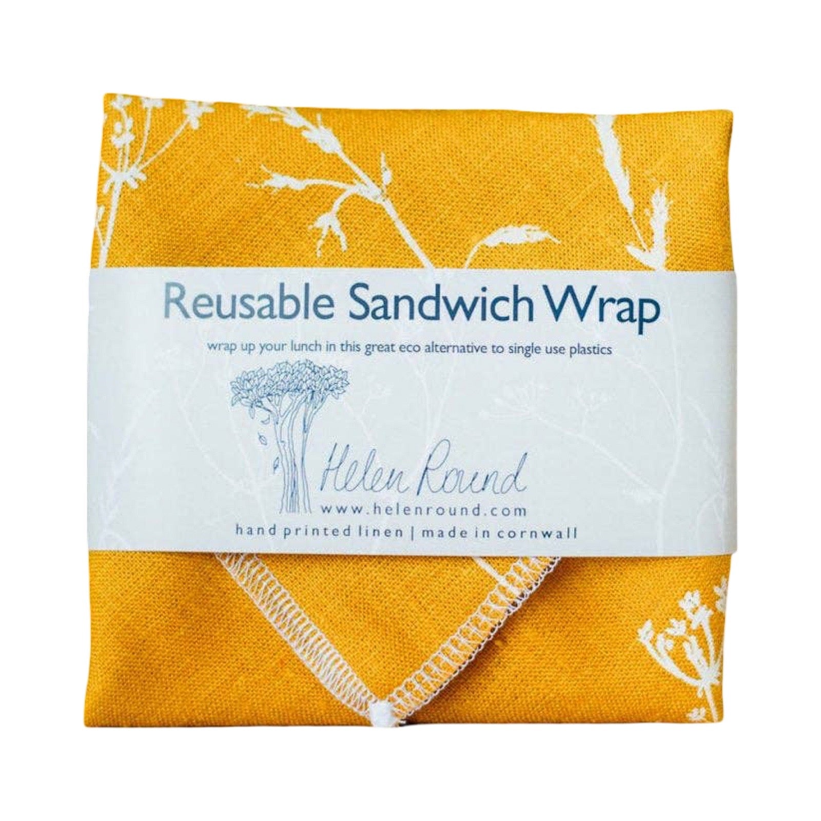 A folded reusable sandwich wrap in mustard yellow linen with white botanical line art, wrapped in a white paper band labeled 'Reusable Sandwich Wrap' and 'Helen Round'.