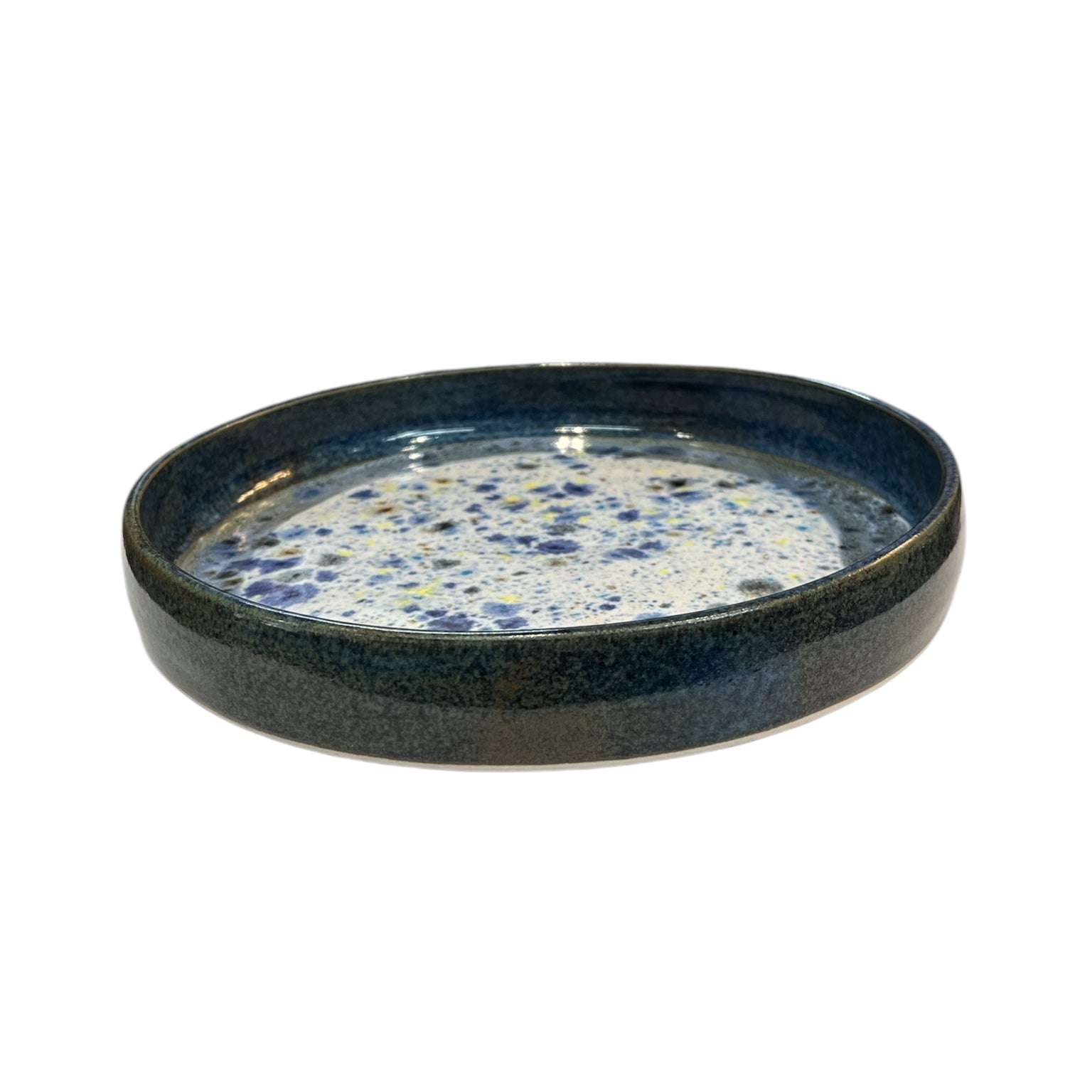 Photo of a handmade ceramic pasta bowl from the side. It has a speckled, white, blue and yellow interior, with navy sides.