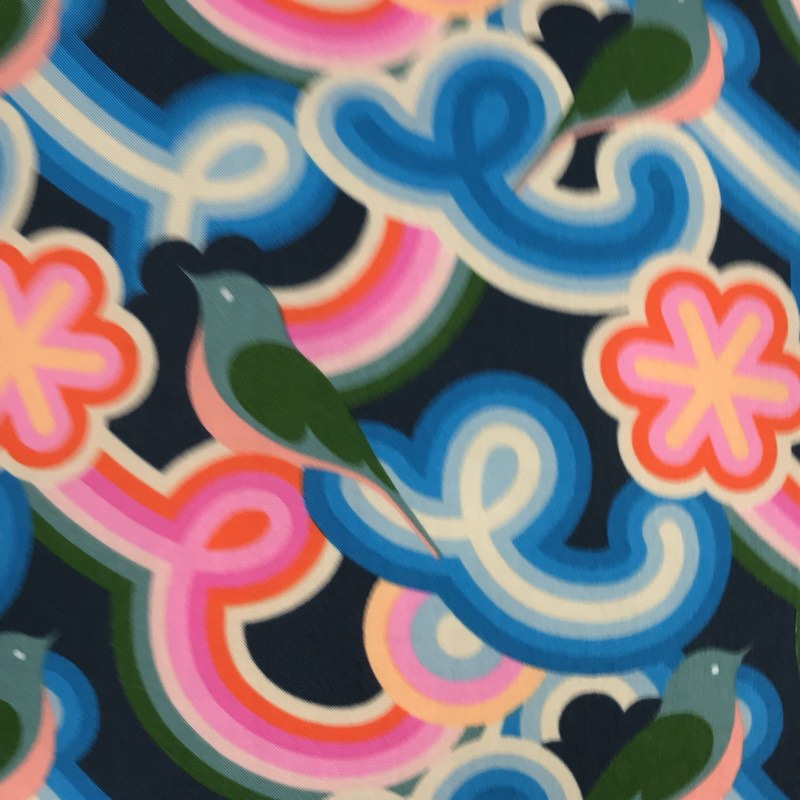 A cushion cover with a geometric pattern featuring navy background and vibrant swirly shapes in pink, blue, and red, along with green birds.