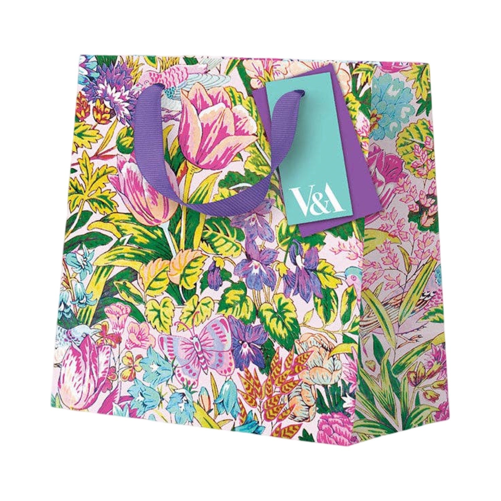 A square paper gift bag with a vibrant, multicolour botanical print featuring pink tulips, purple flowers, green leaves, and butterflies. The bag has purple handles and a teal paper tag with the white text 'V&A'.